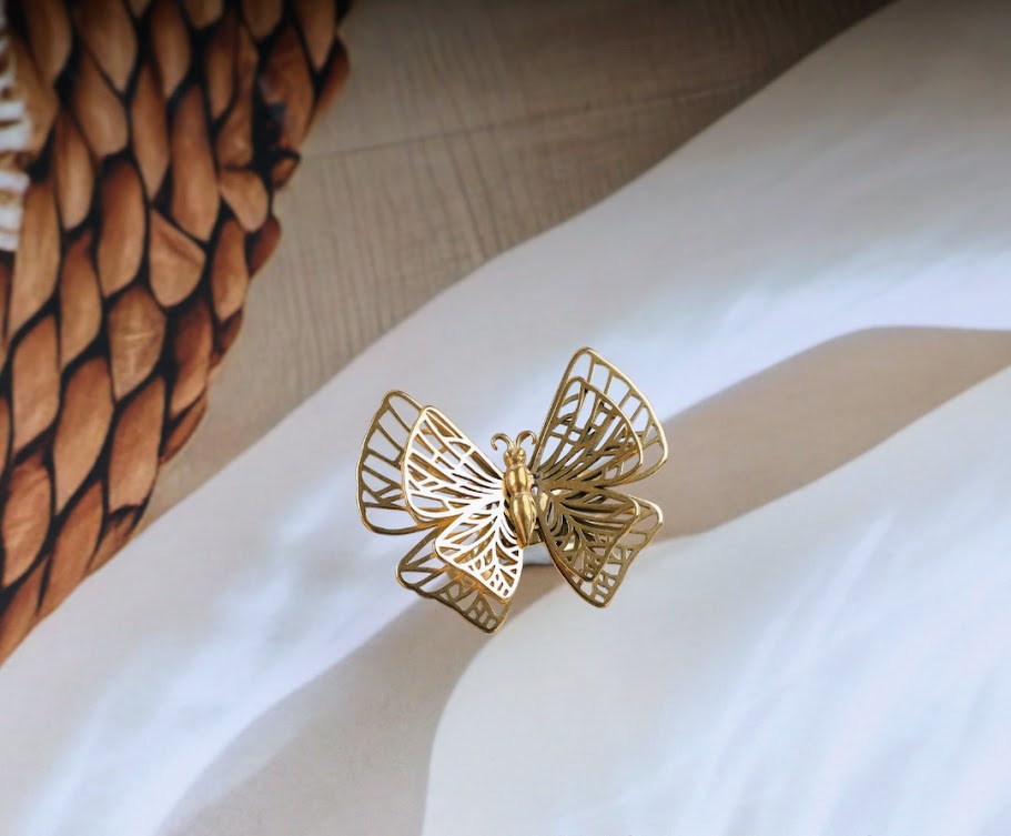 Golden butterfly decorative object with a filigree pattern, presented on a white cloth surface.