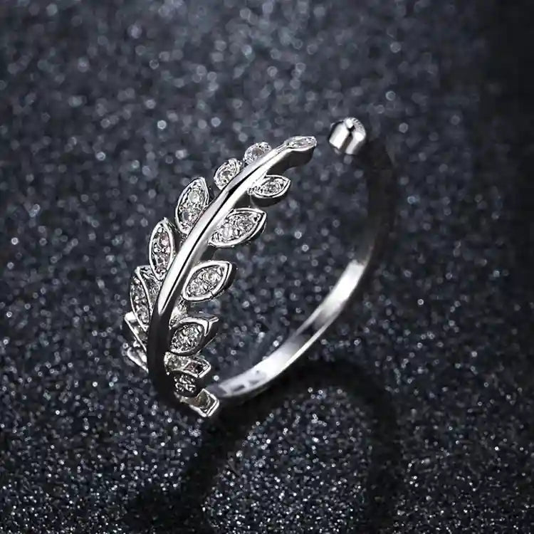 Silver ring featuring a leaf design adorned with small, clear stones on a dark, textured background.