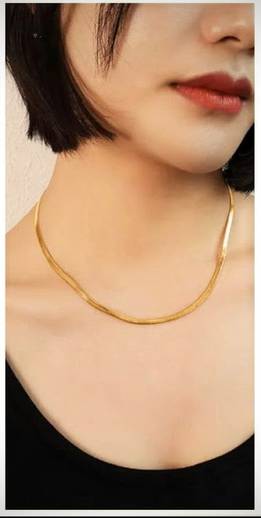 Close-up of a woman wearing a gold herringbone chain necklace.