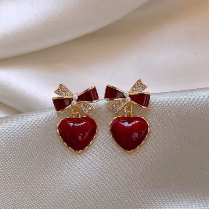 Red heart earrings with bow detail, gold accents.