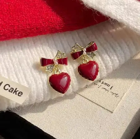 Red heart earrings with bow detail, dangling style.