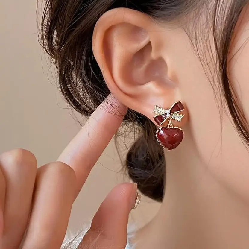 Close-up of a woman wearing red heart-shaped earrings with a bow detail.