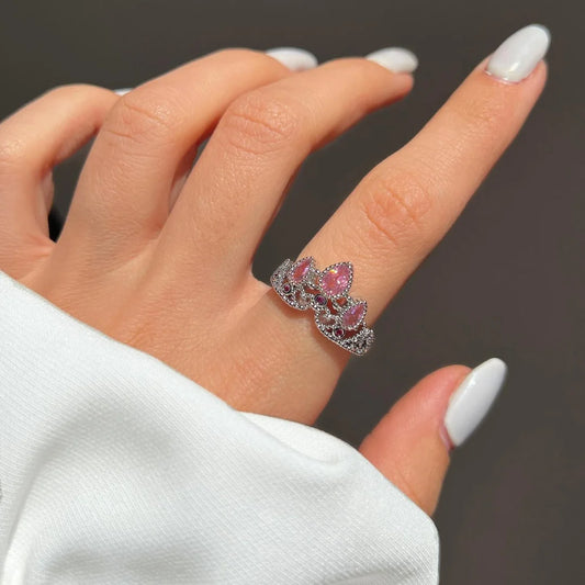 Crown ring with pink stones on a finger. Silver band, tiara design.