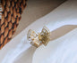 Golden butterfly decorative object with a filigree pattern, presented on a white cloth surface.