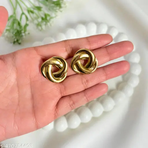 Gold knot stud earrings in hand. Close-up of twisted metal design jewelry.