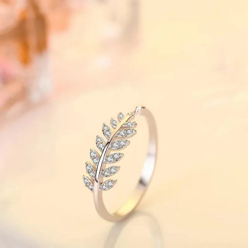 Close up of a silver ring with a leaf design and small clear stone accents.
