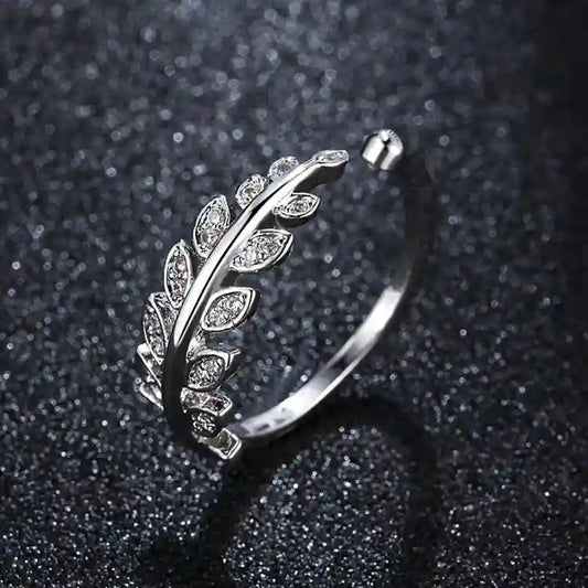 Silver ring featuring a leaf design adorned with small, clear stones on a dark, textured background.