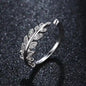 Silver ring featuring a leaf design adorned with small, clear stones on a dark, textured background.