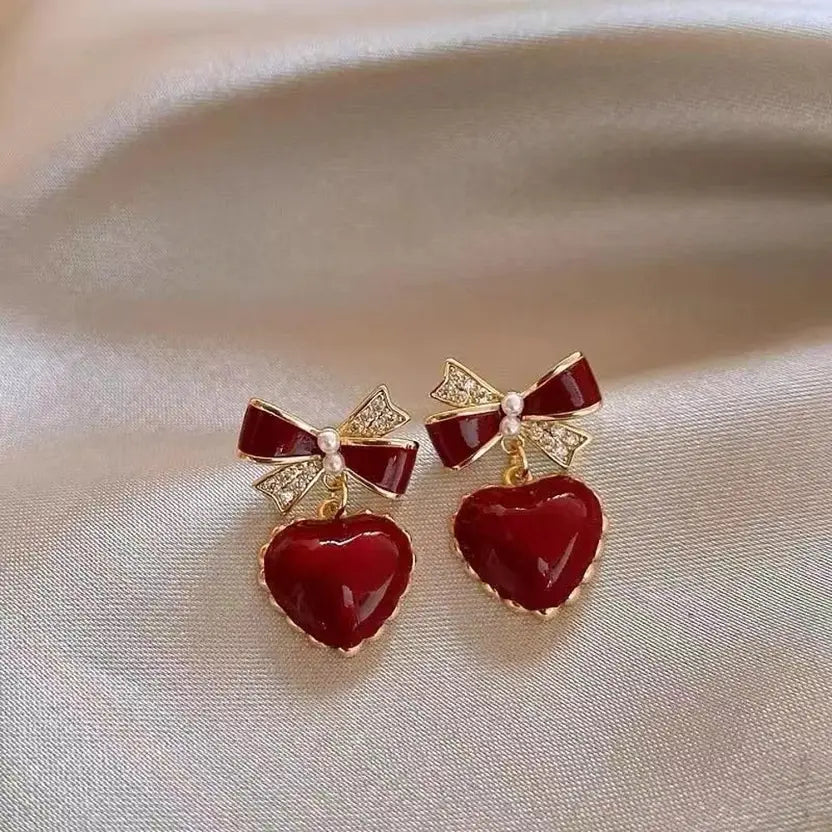 Red heart earrings with bow. Dangle earrings with gold trim and rhinestone details.